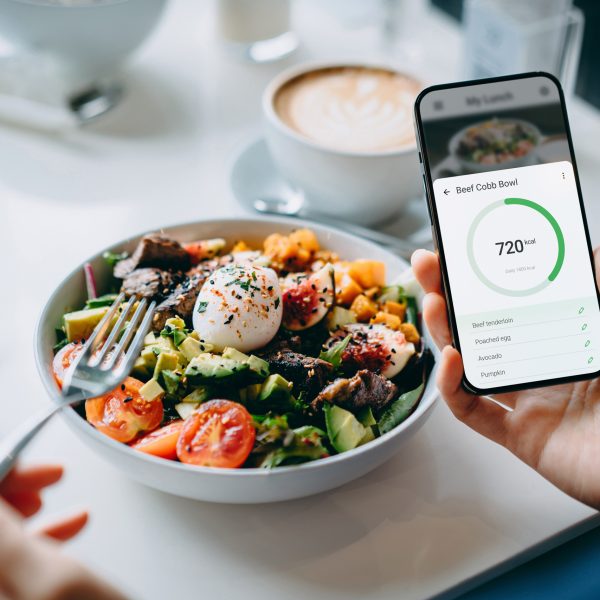 Eine Person sitzt vor einer Bowl und h&auml;lt ein Smartphone in der Hand.