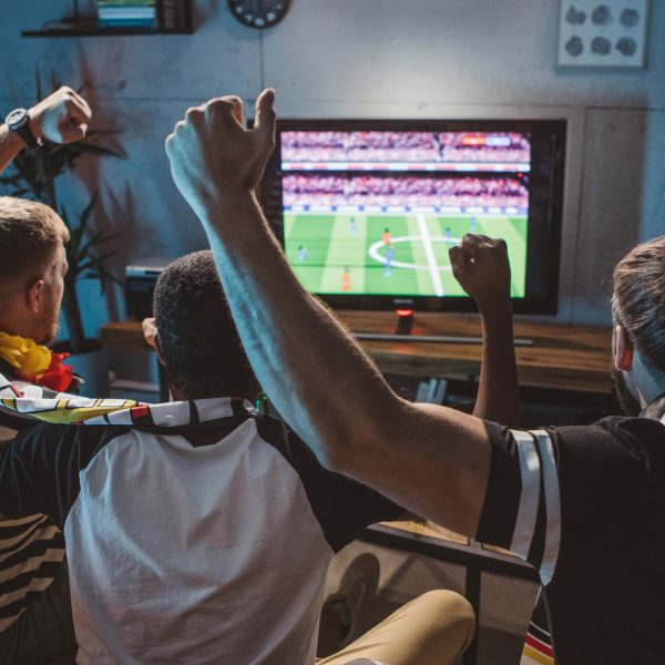 Drei Personen sitzen vor einem Fernseher und schauen ein Fußballspiel.