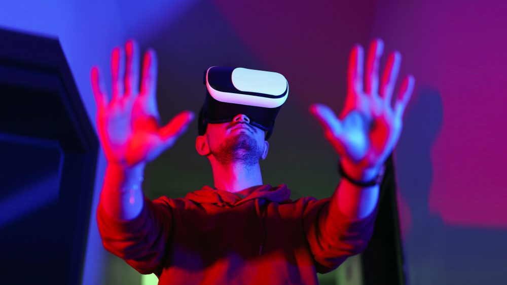 Eine Person steht mit einer VR-Brille in einem Raum und hält ihre Hände hoch.