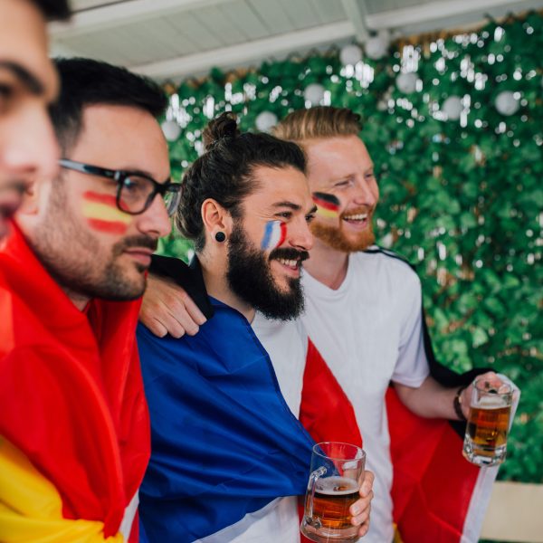 Vier Personen mit L&auml;nderfahnen schauen in Richtung eines nicht sichtbaren Fernsehers.