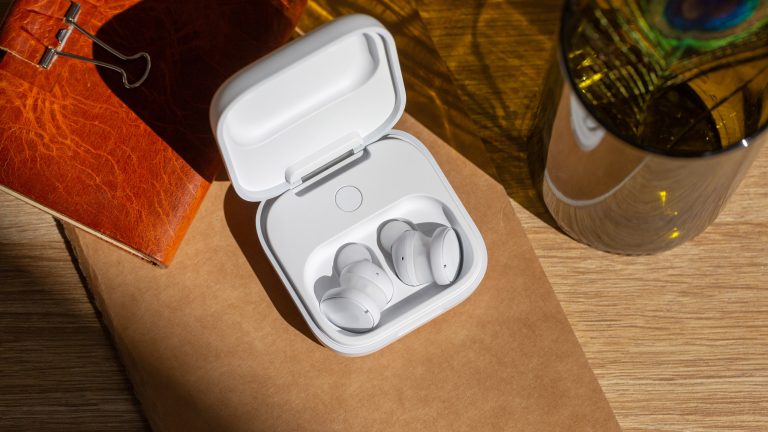 Die Fairbuds liegen im offenen Ladecase auf einem Tisch neben einem ledernen Notizbuch.