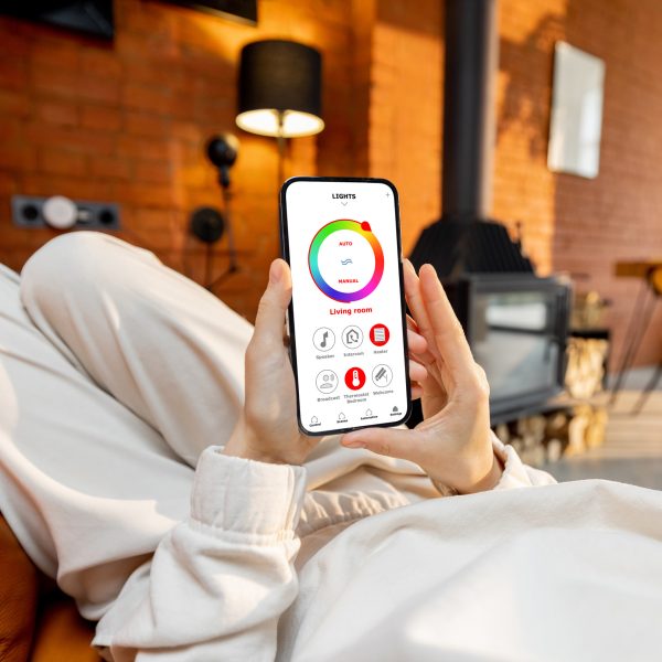 Eine Person h&auml;lt ein Smartphone in der Hand, auf der die App-Steuerung von smarter Beleuchtung zu sehen ist.