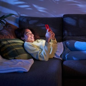 Eine Person liegt im dunklen Wohnzimmer auf der Couch und scrollt an ihrem Handy.