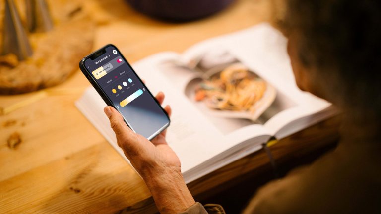 Eine Person h&auml;lt ein Smartphone in der Hand, auf der die Lichtsteuerung smarter Beleuchtung zu sehen ist.