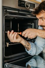 Eine Person in einem Blaumann schraubt an einem Elektroherd.