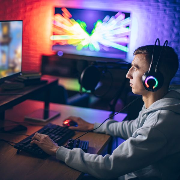 Eine Person sitzt vor einem Gaming Set-up mit bunten LED-Lichtern im Hintergrund.
