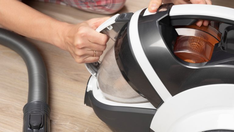 Eine Person nimmt den Staubbehälter aus ihrem Staubsauger.