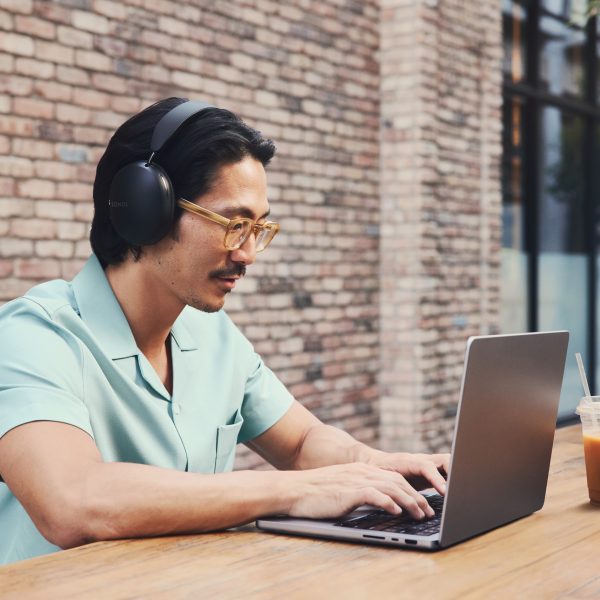 Eine Person sitzt an einem MacBook Pro und tr&auml;gt dabei Sonos Ace in Schwarz.
