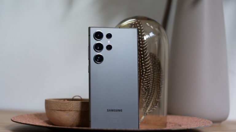 Ein Samsung Galaxy S24 Ultra steht mit der Rückseite zur Kamera in einer Schale neben diversen Deko-Objekten. Ein Samsung Galaxy S24 Ultra steht mit der Rückseite zur Kamera in einer Schale neben diversen Deko-Objekten.