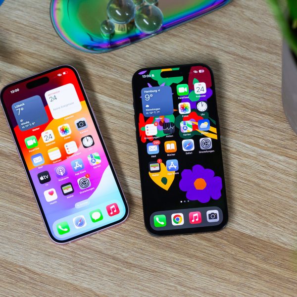 Auf einem Holztisch liegen ein iPhone 15 Pro und ein iPhone 15 nebeneinander. Auf dem eingeschalteten Display ist die Dynamic Island bei beiden Geräten zu erkennen.