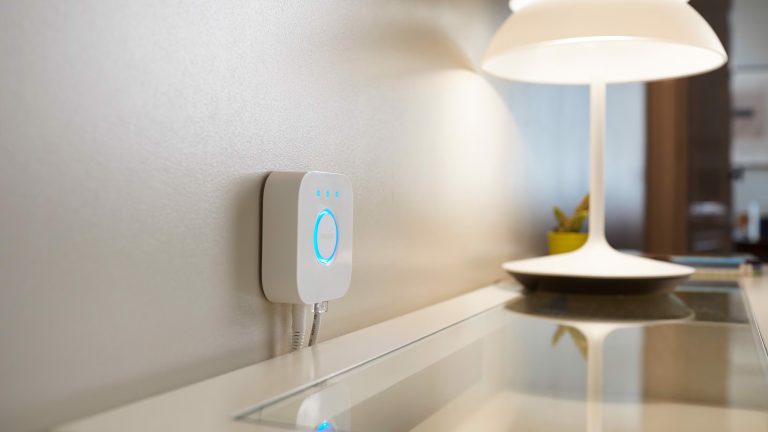 Eine Hue Bridge ist nahe einer Tischleuchte an einer Wand angebracht.