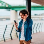 Eine Person h&ouml;rt drau&szlig;en Musik und h&auml;lt dabei ihr Smartphone in der Hand.