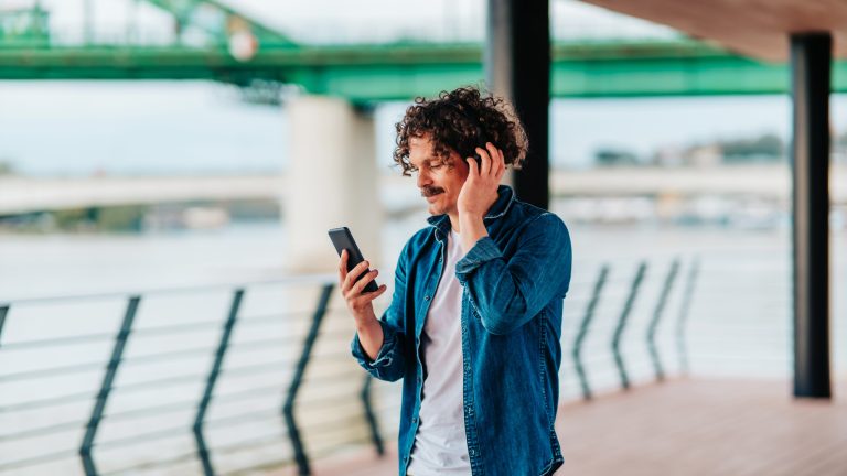 Eine Person hört draußen Musik und hält dabei ihr Smartphone in der Hand.