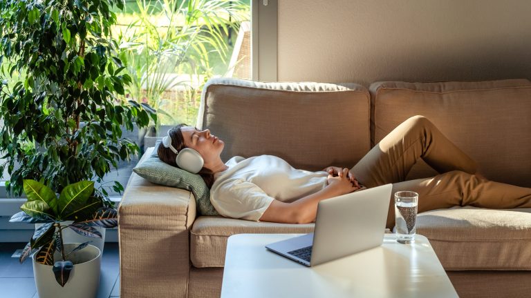 Eine Person liegt auf einem Sofa und hört über Kopfhörer Musik von einem verbundenen Laptop.