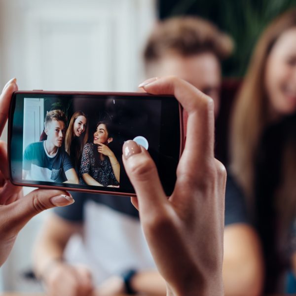 Eine Person macht mit dem Smartphone ein Foto von drei anderen Personen.