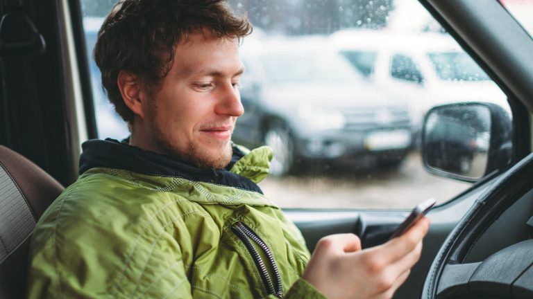 Eine Person sitzt mit dem Smartphone in der Hand in einem &auml;lteren Auto.