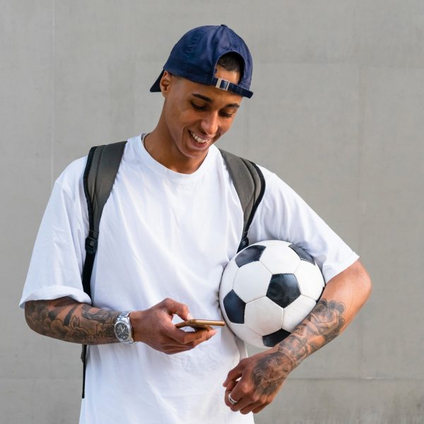 Eine Person mit einem Fu&szlig;ball unter dem Arm schaut auf ihr Smartphone.
