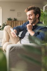 TikTok Coins, so lädst du sie auf und verteilst Geschenke Eine Person sitzt in einem Wohnzimmer mit vielen Pflanzen auf der Couch und scrollt auf ihrem Smartphone.