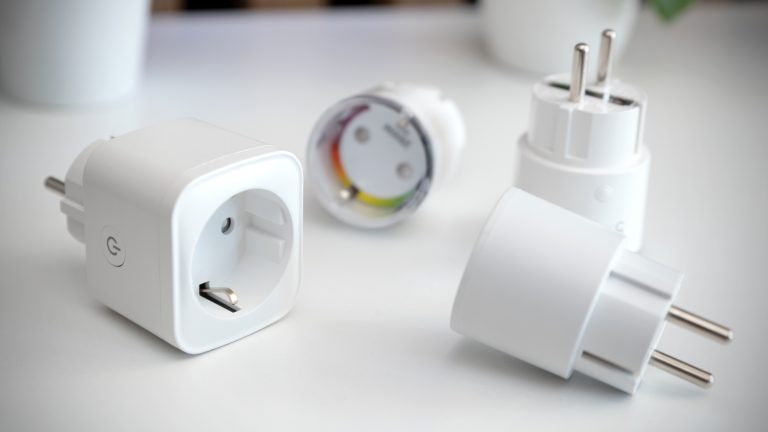 Vier smarte Steckdosen liegen auf einem Tisch nebeneinander.