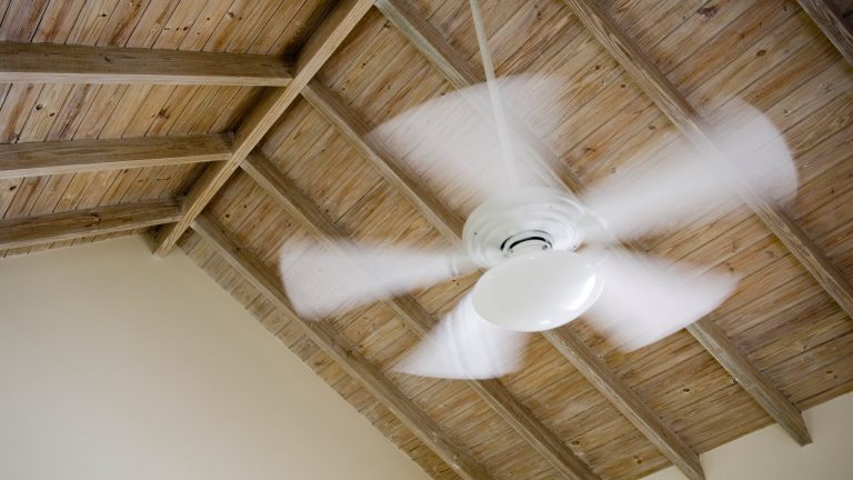 Ein Deckenventilator hängt von einem Holzdach und dreht sich.