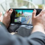 Eine Person spielt etwas auf einem Steam Deck LCD, daneben h&auml;lt jemand ein Steam Deck OLED in der Hand.