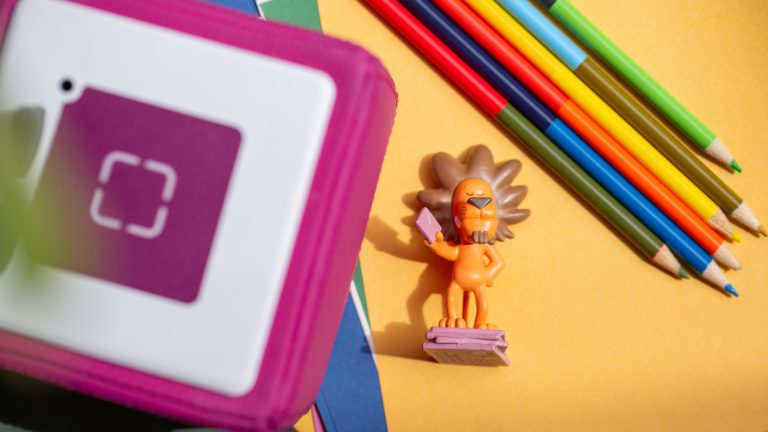 Ein Löwen-Tonie liegt auf einem Blatt Papier neben einer Toniebox.