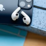 Zwei AirPods liegen auf der Rückseite von einem iPhone.
