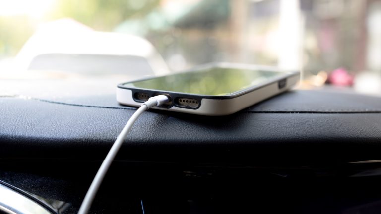 Ein iPhone liegt angesteckt an ein Auto auf dessen Armaturenbrett.