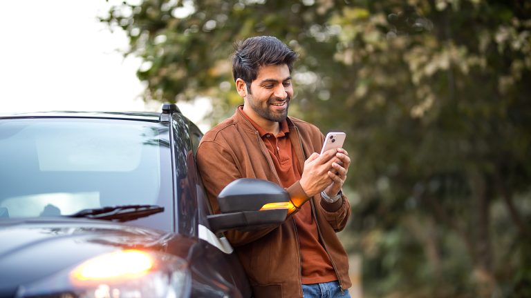 Eine Person steht neben einem Auto, bei dem die Blinker leuchten und hält ein iPhone in der Hand.