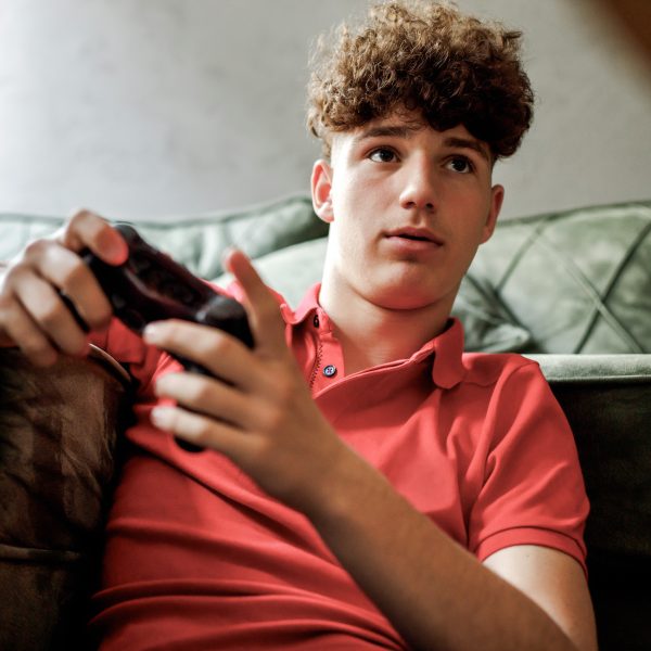 Eine Person mit einem Controller in der Hand sitzt vor einem Sofa.