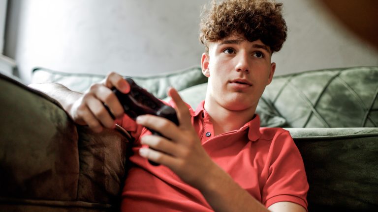 Eine Person mit einem Controller in der Hand sitzt vor einem Sofa.