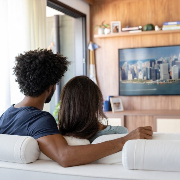 Ein P&auml;rchen sitzt im Wohnzimmer auf der Couch und sieht auf einem Fernseher fern.&nbsp;