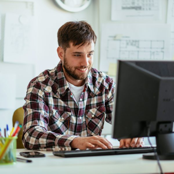 Eine Person sitzt l&auml;chelnd in einem B&uuml;ro vor einem Rechner.