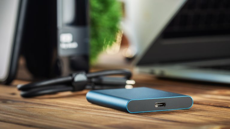 Eine externe Festplatte liegt mitsamt Kabel neben einem Laptop.