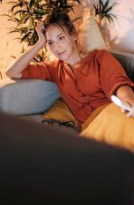 Zattoo, Live-TV, Kosten, Aufnahmen & mehr Eine Person liegt auf einem Sofa vor einem Fernseher und hält eine Fernbedienung in der Hand.