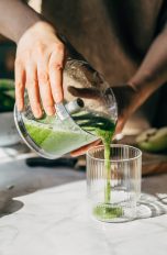 Eine Person gie&szlig;t zerkleinertes Obst und Gem&uuml;se von einem Zerkleinerer in ein Glas.