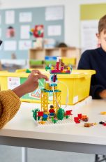 Zwei Kinder spielen an einem Tisch mit LEGO Spike. Eines davon bedient dabei ein Tablet.