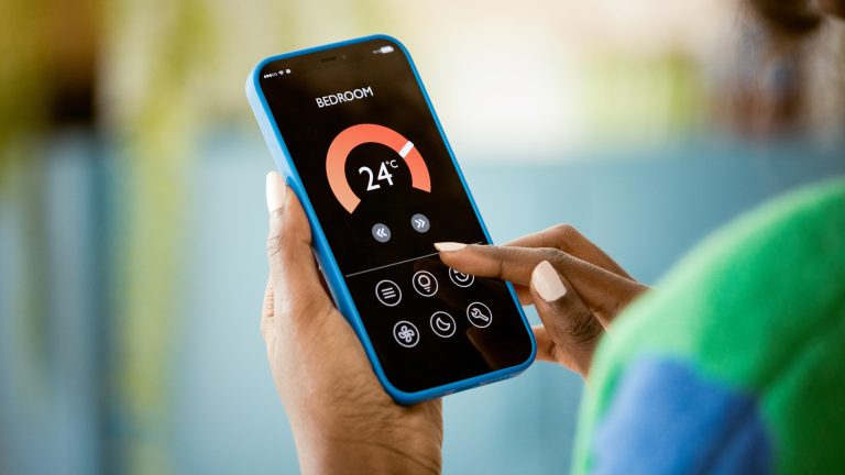 Eine Person h&auml;lt ein Smartphone in der Hand, das eine Temperaturanzeige und Einstellungsm&ouml;glichkeiten f&uuml;r ein Schlafzimmer anzeigt.