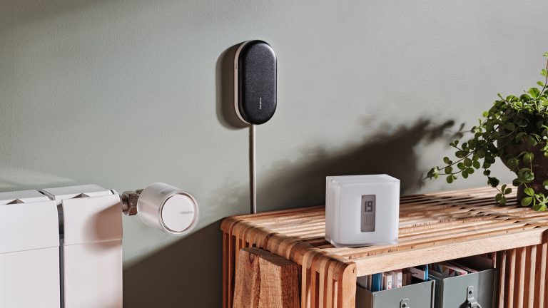 Neben einer Heizung mit smartem Thermostat am Regler, sieht man eine freistehende Temperaturanzeige auf einem Sideboard und ein weiteres smartes Ger&auml;t an der Wand dahinter.