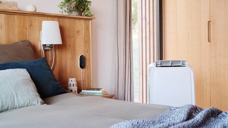 Ein kleines freistehendes Klimager&auml;t steht in einem Schlafzimmer neben einem Bett.