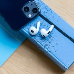 Zwei AirPods liegen neben einem iPhone auf einem Notizbuch.