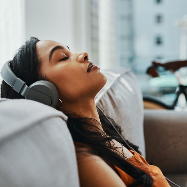 Eine Person sitzt auf einem Sofa, lehnt sich zur&uuml;ck und h&ouml;rt &uuml;ber Kopfh&ouml;rer Musik.