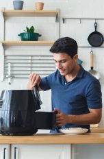 Airfryer - welche gibts. Philips, tefal, ninja Eine Person steht in der Küche und holt etwas aus einem Airfryer. Daneben steht auf der Küche ein Laptop.