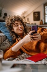 Clear Mode Tiktok, So erreichst du den aufgeräumten Look Eine Person liegt auf der Couch im Wohnzimmer mit Pflanzen im Hintergrund und scrollt auf ihrem Smartphone.