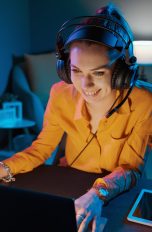 Eine Person mit einem Headset auf dem Kopf sitzt vor einem Laptop.