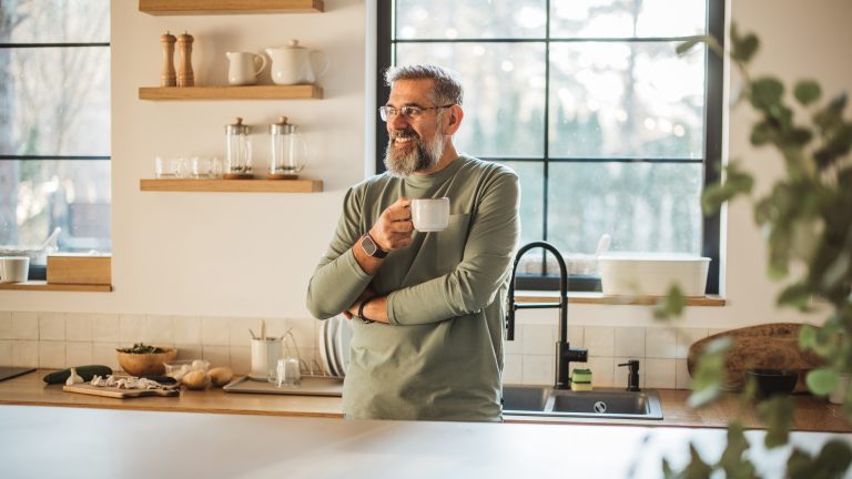 Eine Person steht mit einer Kaffeetasse angelehnt an der Küchentheke.