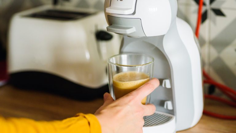 Eine Person nimmt einen frischen Kaffeebecher vom Becherhalter einer Dolce Gusto Maschine.