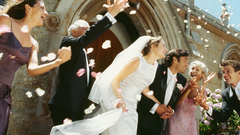 Ein Hochzeitspaar kommt aus einer Kirch. Die Hochzeitsgemeinschaft wirft Bl&uuml;ten in die Luft.