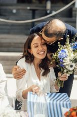 Geschenke zur Hochzeit, Ideen für frisch Vermählte Ein Hochzeitspärchen sitzt an einem Tisch und nimmt ein Geschenk in Empfang.