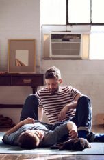 Klimaanlage, Diese Typen gibt es, dann lohnt sie sich Zwei Personen und eine Katze entspannen auf einem Teppich. Im Hintergrund ist eine Split-Klimaanlage zu sehen.